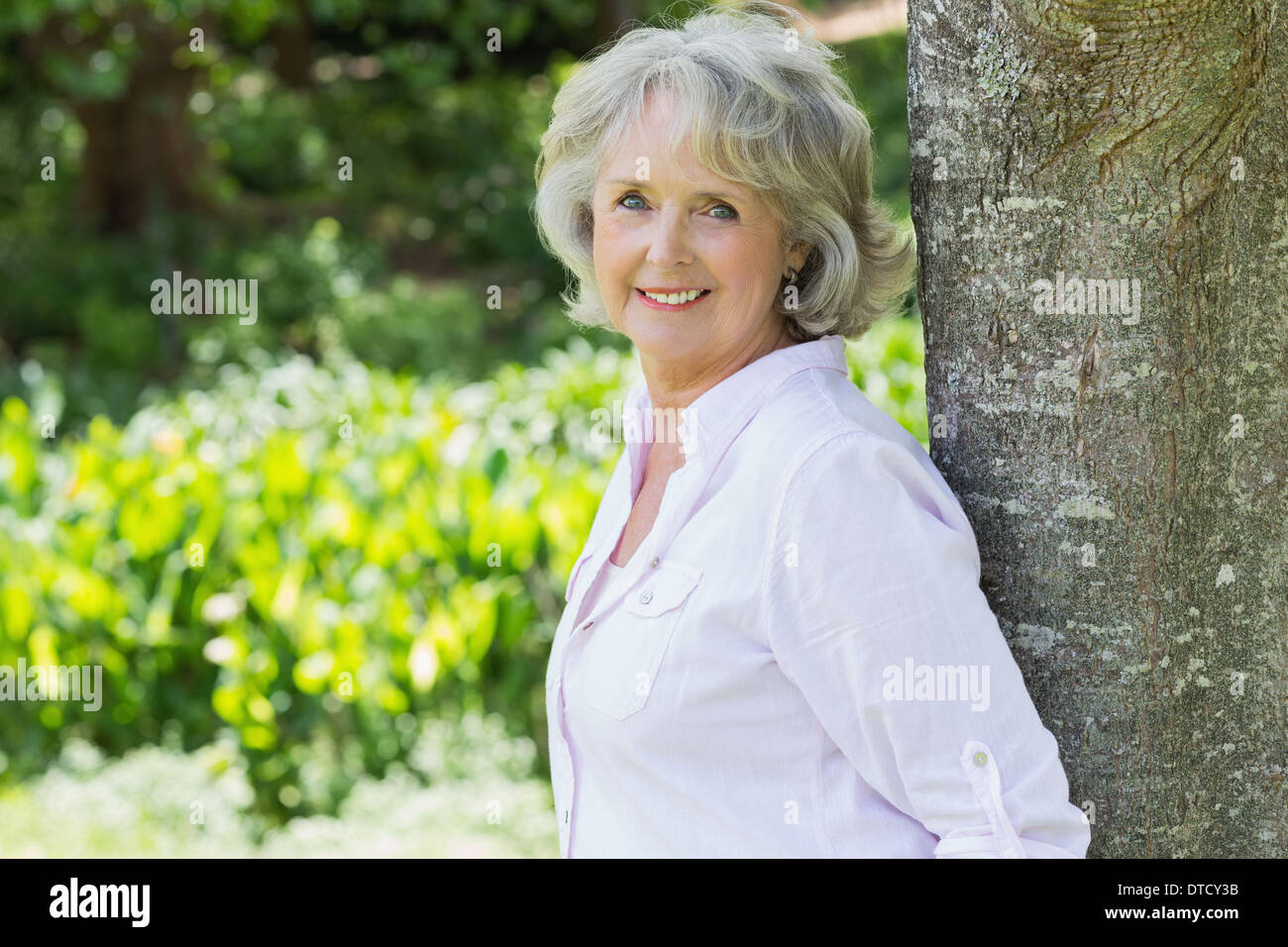 Ritratto di una donna matura appoggiato contro il tronco di albero Foto Stock