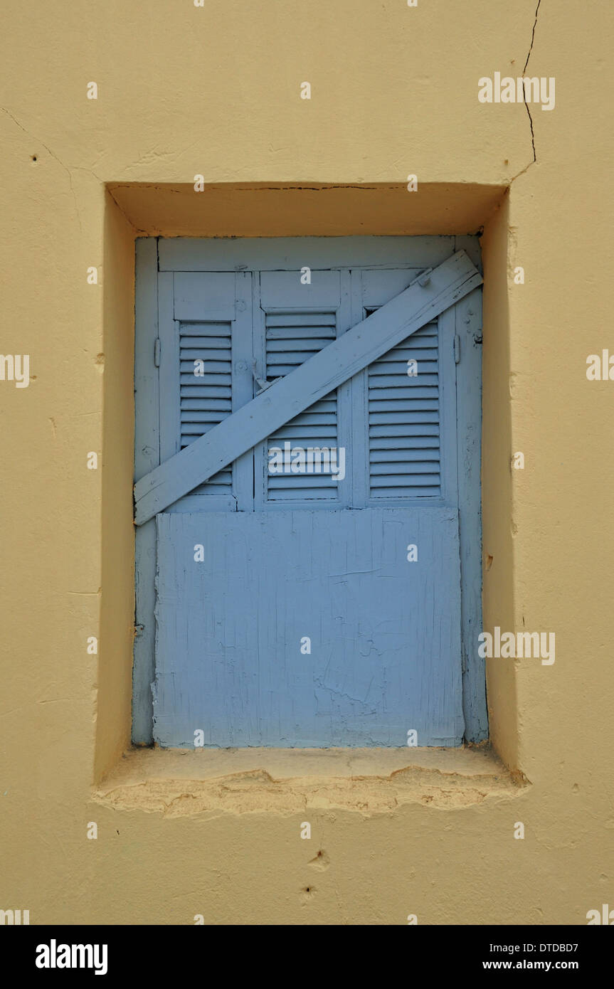 Finestra blu shutter e giallo parete incrinata. Saliti fino casa abbandonata esterno. Foto Stock