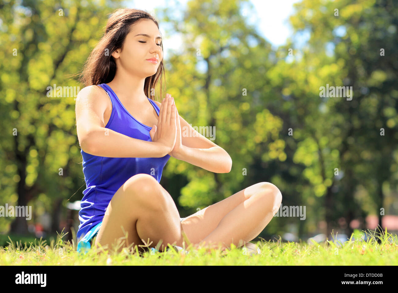 Giovane atleta femminile in sportswear facendo esercizi yoga seduto su un prato in un parco Foto Stock