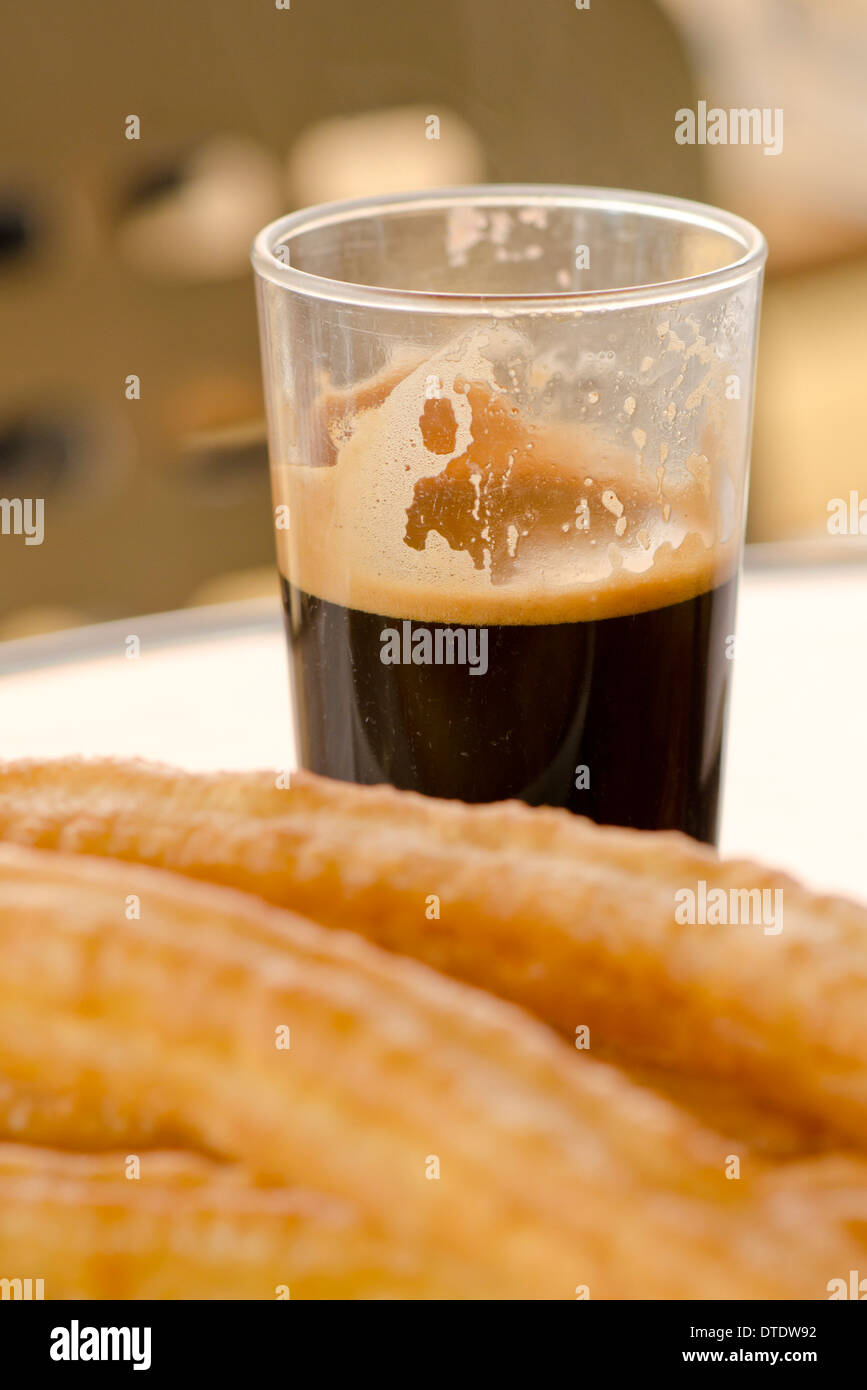 Tazza di nero caffè spagnolo dietro alcuni Churros (Porra) su una piastra bianca, senza zucchero aggiunto. Andalusia, Spagna. Foto Stock