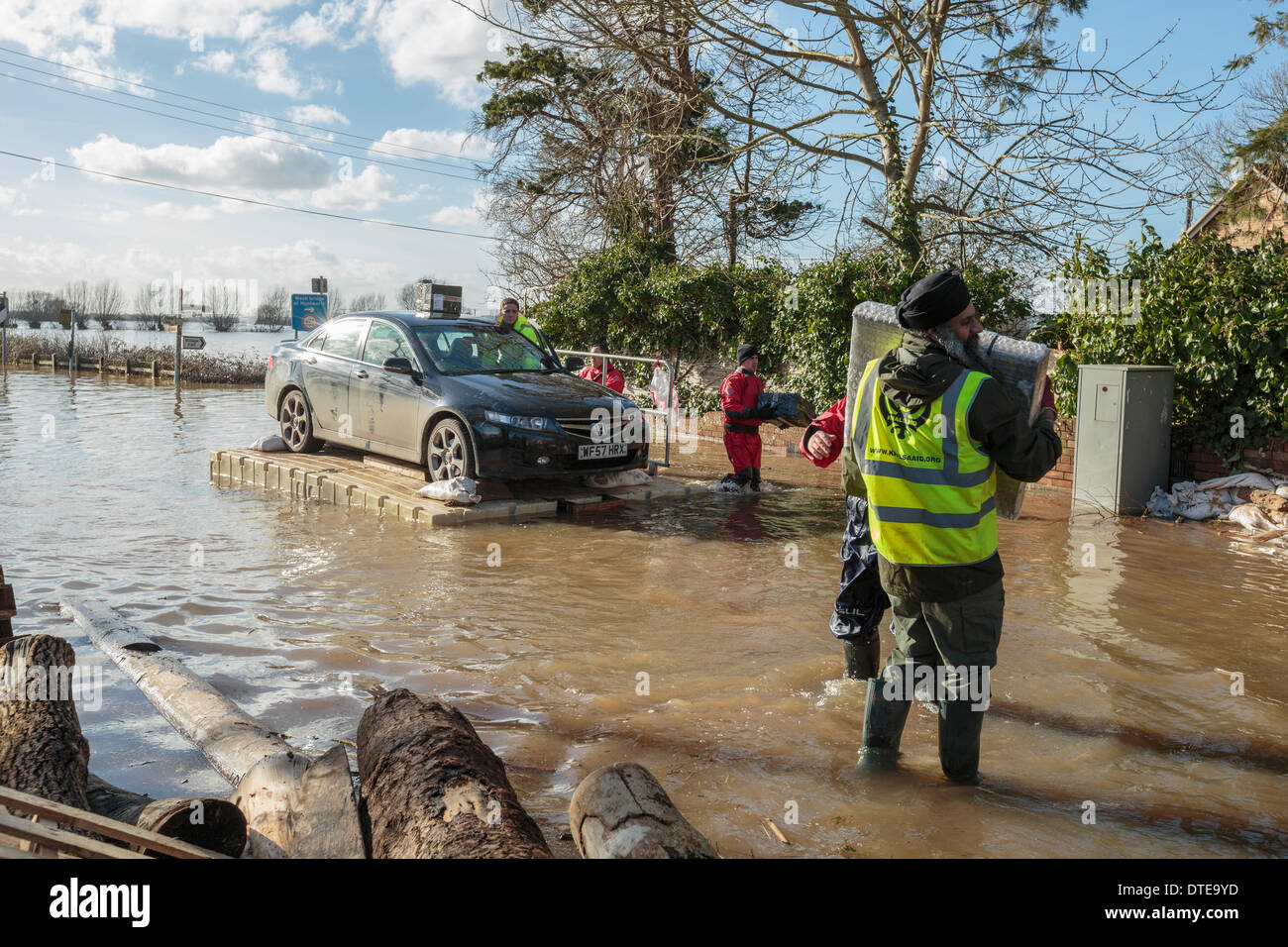 Burrowbridge, UK. 16 feb 2014. Volontari il salvataggio di una Honda Accord durante forti inondazioni sui livelli di Somerset il 16 febbraio 2014. La vettura è stata piena di cose e guidato su un pontone utilizzati per il trasporto di veicoli e di bestiame e di aiuti nella Comunità allagata. Un membro dei khalsa organizzazione di aiuti porta cassette di sicurezza. A361 è un importante arteria attraverso la Somerset livelli e ha appena vissuto la peggiore inondazione nella storia viva e è stato adesso subacqueo per sette settimane. Credito: Nick Cable/Alamy Live News Foto Stock