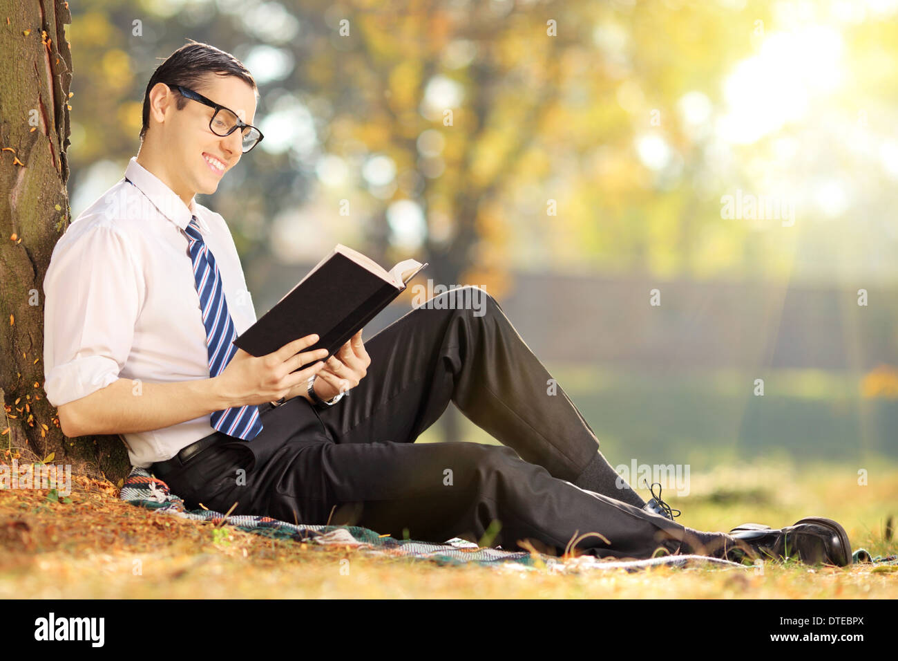 Giovane maschio seduti sul prato verde e la lettura di un libro in posizione di parcheggio Foto Stock
