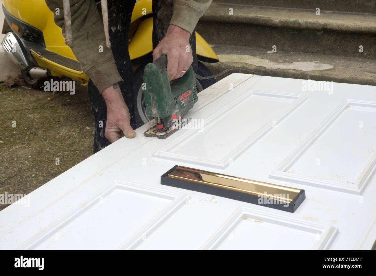 Tradesman all'opera per preparare una nuova porta e il telaio di montaggio sulla parte anteriore di un ambiente domestico Foto Stock
