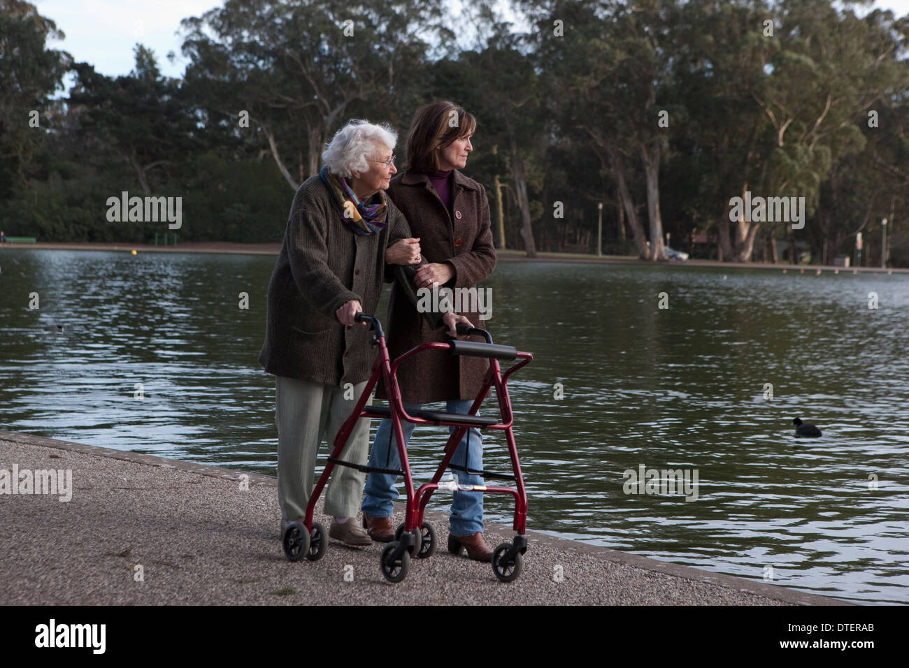 Donna anziana passeggiate intorno al laghetto con caregiver femmina Foto Stock