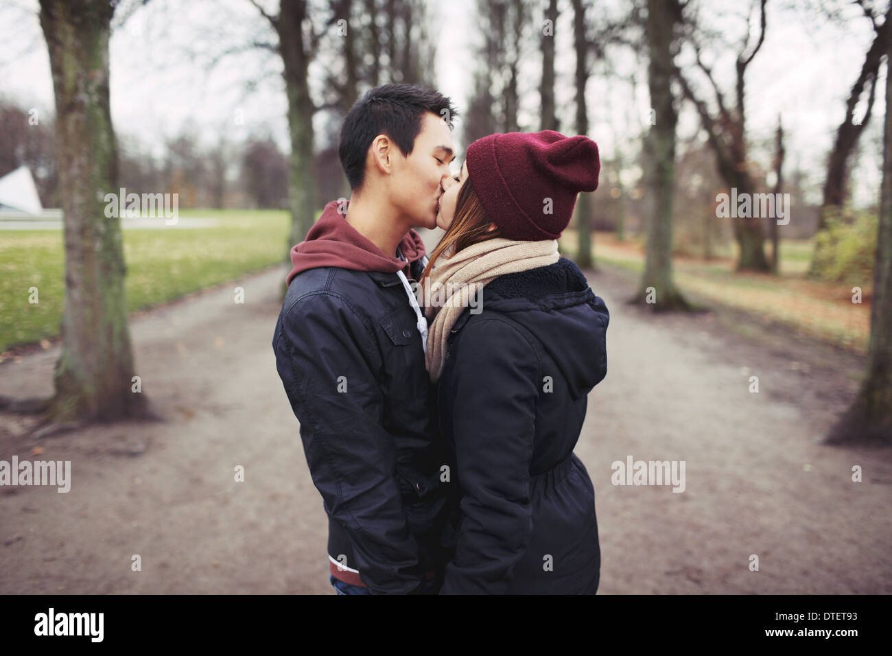Amorevole coppia giovane kissing all'aperto nel parco. Razza mista l uomo e la donna. Amore adolescenziale. Foto Stock