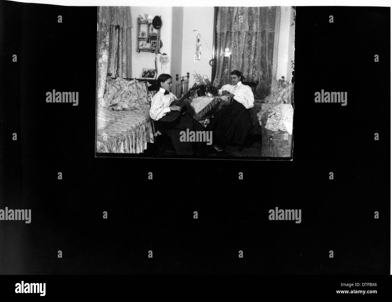La fotografia raffigura due donne in un dormitorio, probabilmente dell'inizio del XX secolo. Cattura un momento della vita quotidiana in un ambiente educativo o sociale, offrendo una visione della vita delle donne durante quel periodo, con strumenti musicali presenti nella stanza. Foto Stock