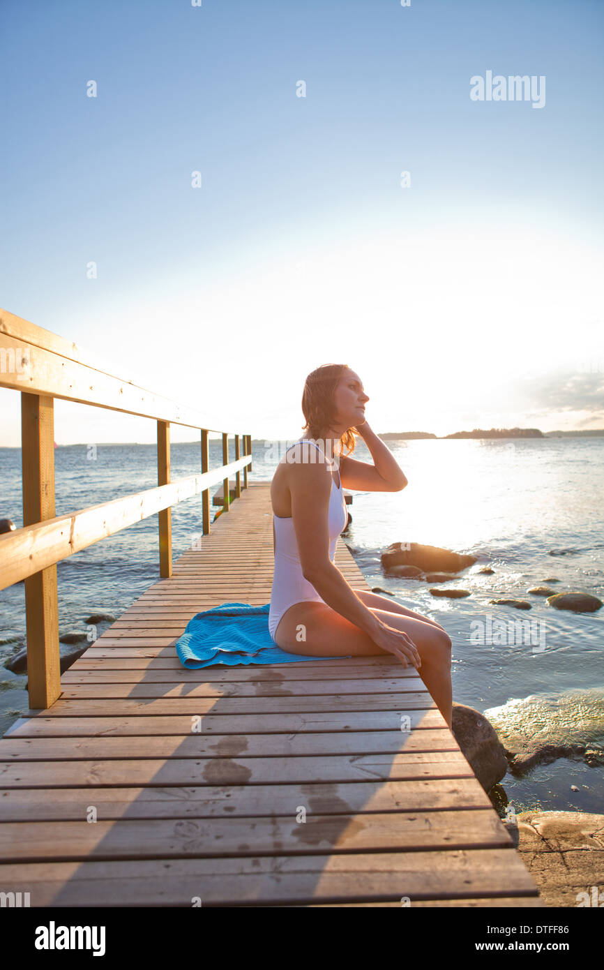 Donna attraente in bianco costume da bagno seduta sul molo in legno nel paese nordico durante l'estate Foto Stock