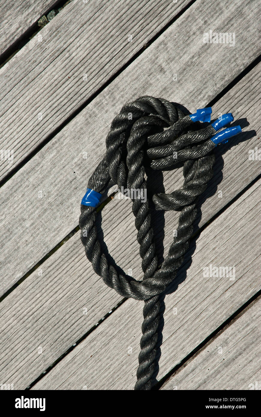 Corda nera con cravatta blu off su assicelle di legno di un pontile Foto Stock