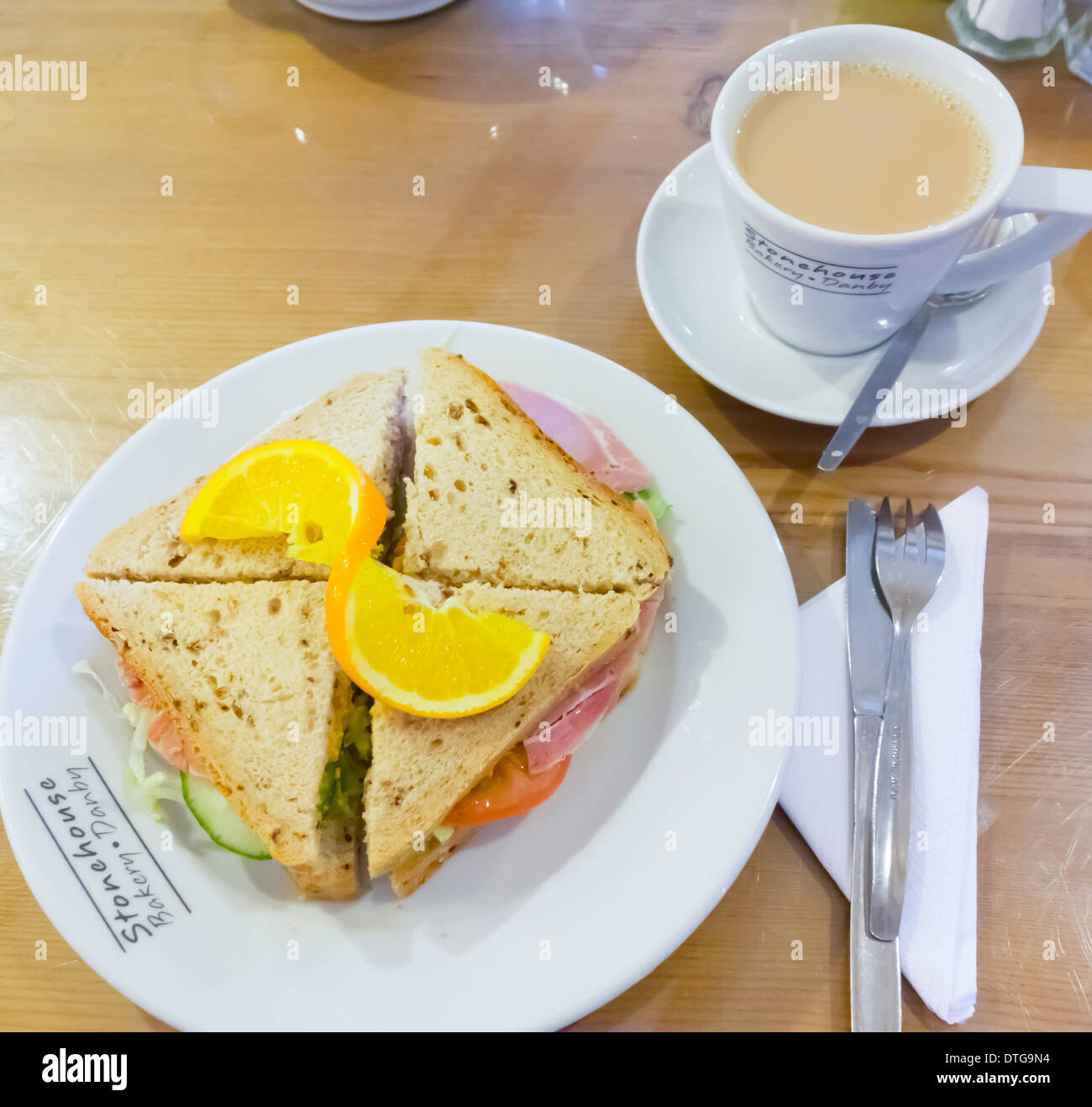 Café pranzo un prosciutto e insalata sandwich in multi-pane di grano con un tocco di colore arancione e una tazza di tè in Stonehouse Bakery Café Foto Stock