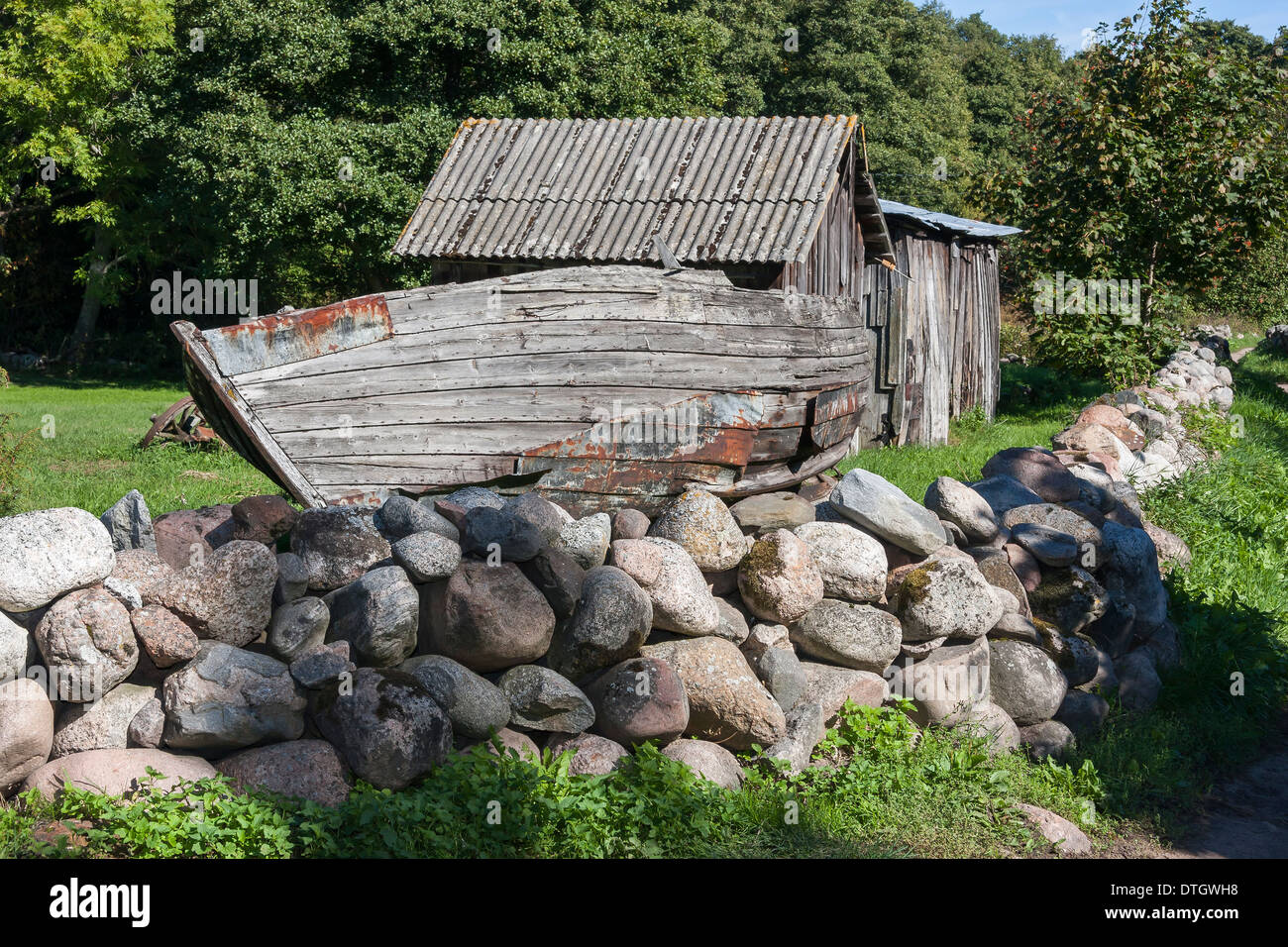 Vecchio grigio rotto la barca di legno nel giardino dietro di ciottoli di recinzione in pietra Foto Stock