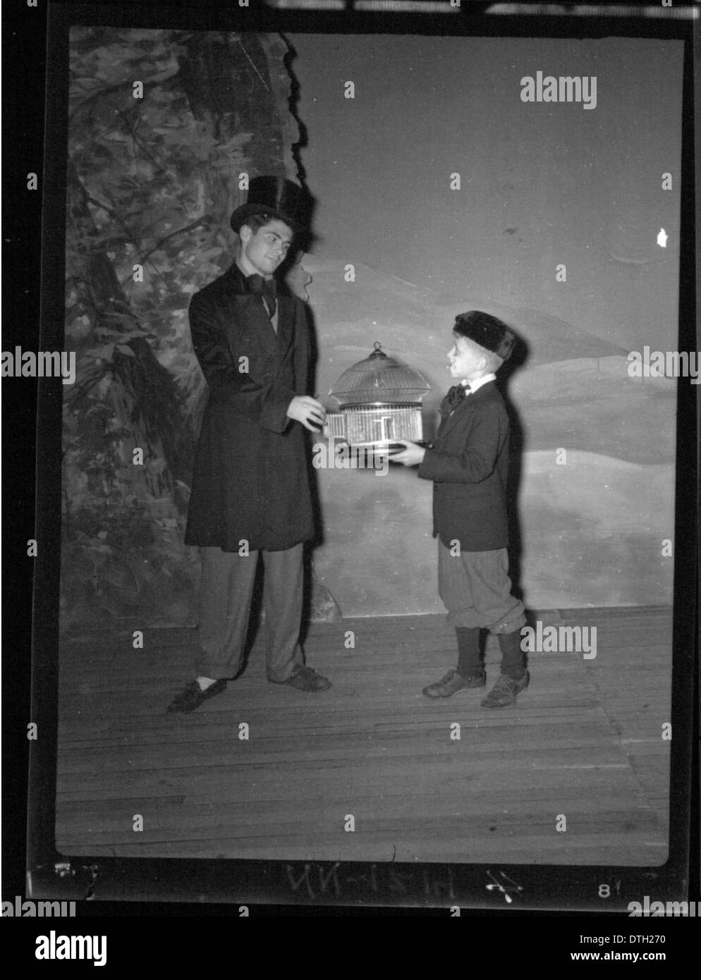 Questa fotografia cattura un uomo e un ragazzo in costumi teatrali sul palco, accompagnati da gabbie per uccelli e oggetti di scena. L'immagine, parte della collezione della Miami University, riflette l'importanza delle produzioni teatrali e dell'educazione femminile nelle prime esecuzioni. Foto Stock