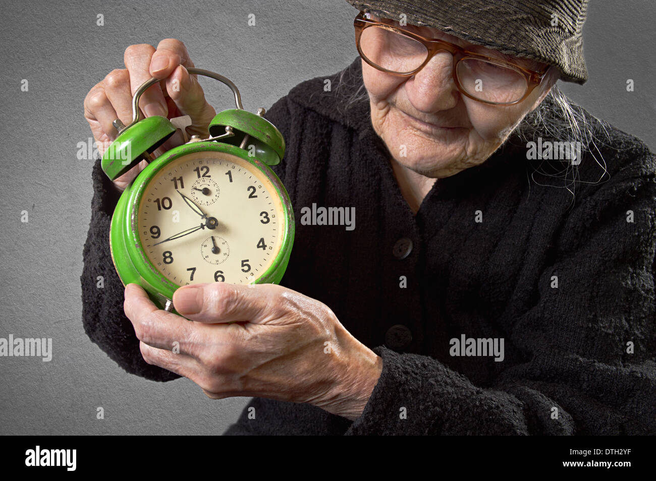 Donna anziana tenendo una sveglia su un sfondo vintage. Foto Stock