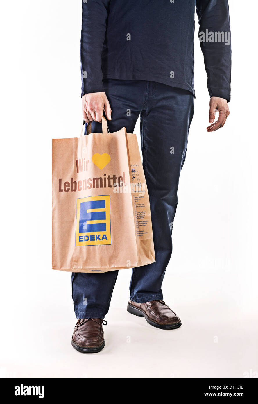 La parte inferiore del corpo di un uomo che indossa un sacchetto di carta della catena alimentare LA EDEKA. Foto Stock