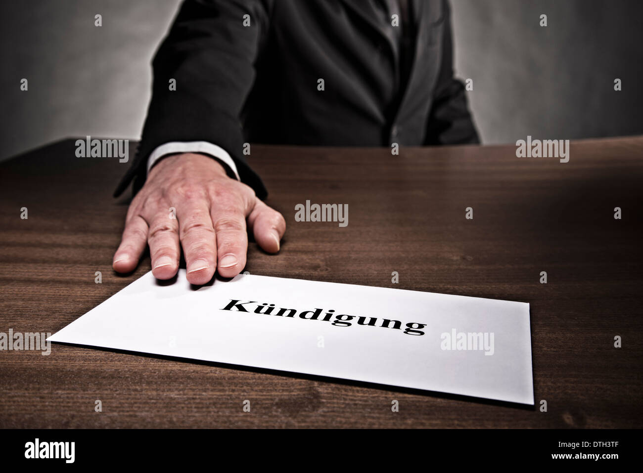 Uomo di mettere una lettera con la cessazione del contratto di lavoro attraverso la scrivania. Foto Stock