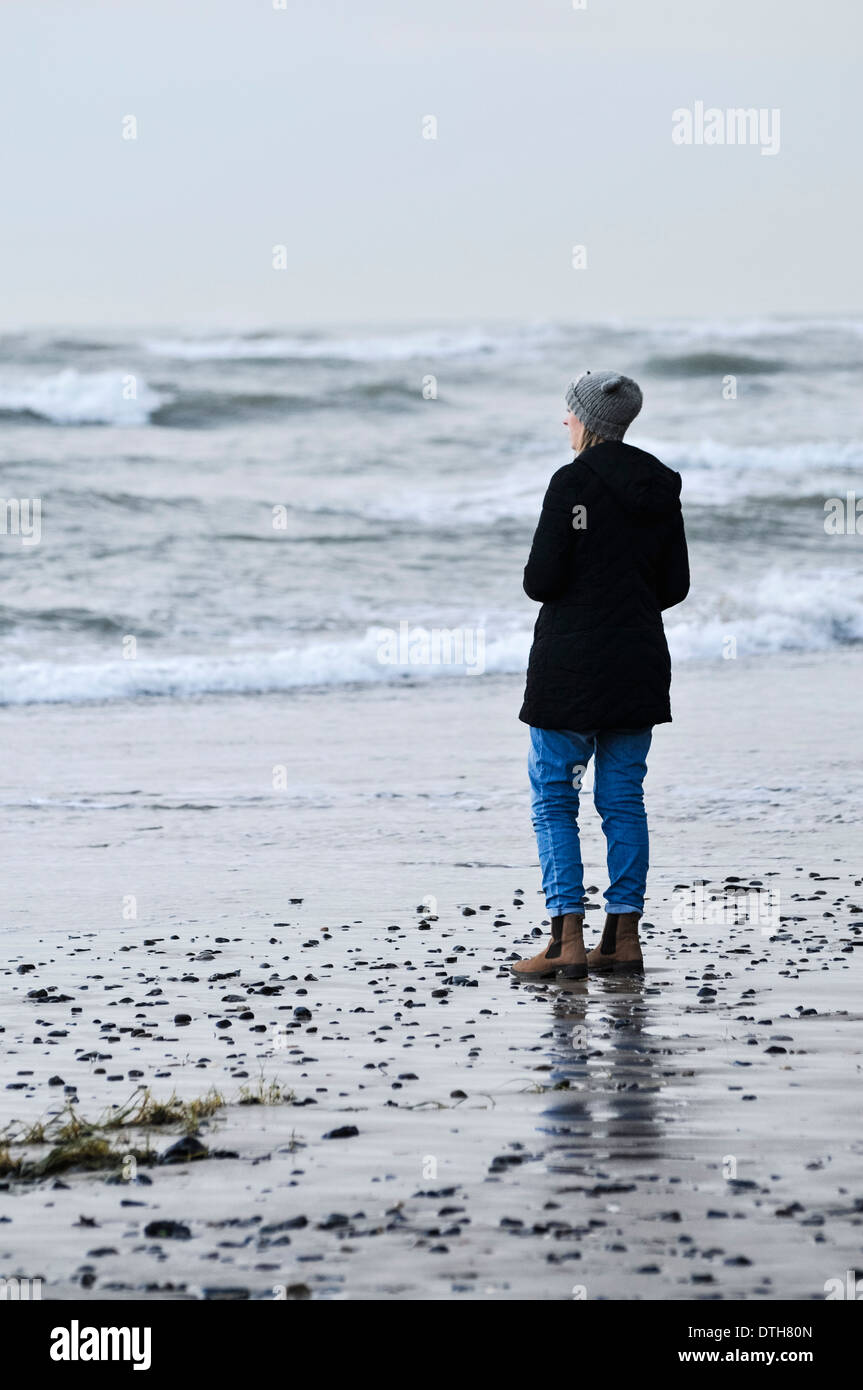 Una donna si trova su una spiaggia e si affaccia sul mare in tempesta Foto Stock