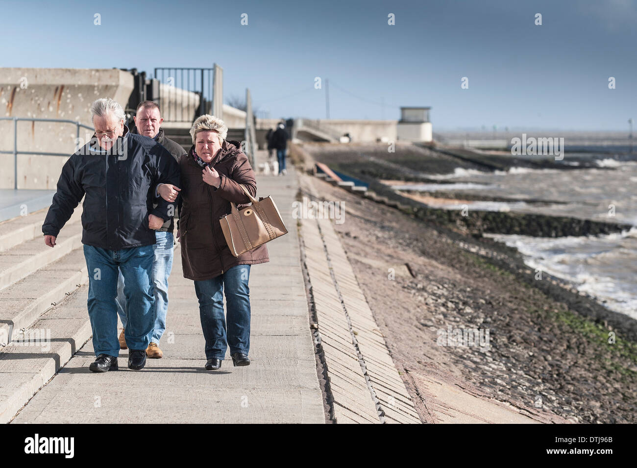La gente camminare contro vento sul mare muro a Canvey Island in Essex. Foto Stock