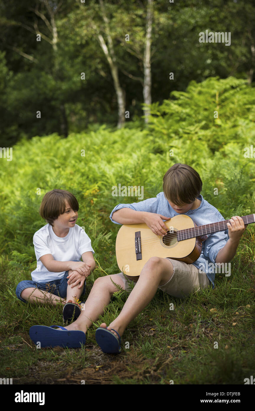 Due ragazzi in campeggio in New Forest seduto sull'erba uno di suonare una chitarra Hampshire Inghilterra Foto Stock