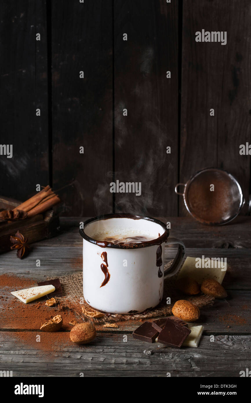 Vintage mug con cottura a vapore caldo cioccolato servito con pezzi di bianco e il cioccolato fondente e mandorle sul vecchio tavolo in legno Foto Stock