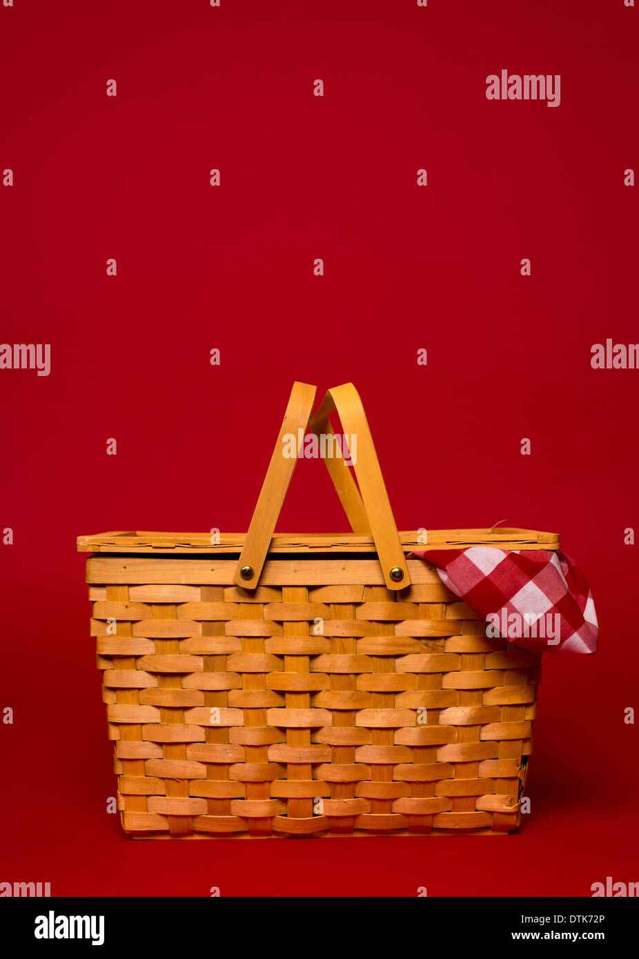 Un marrone, vimini Cesto picnic con rosso Gingham tovaglia su uno sfondo rosso con spazio di copia Foto Stock