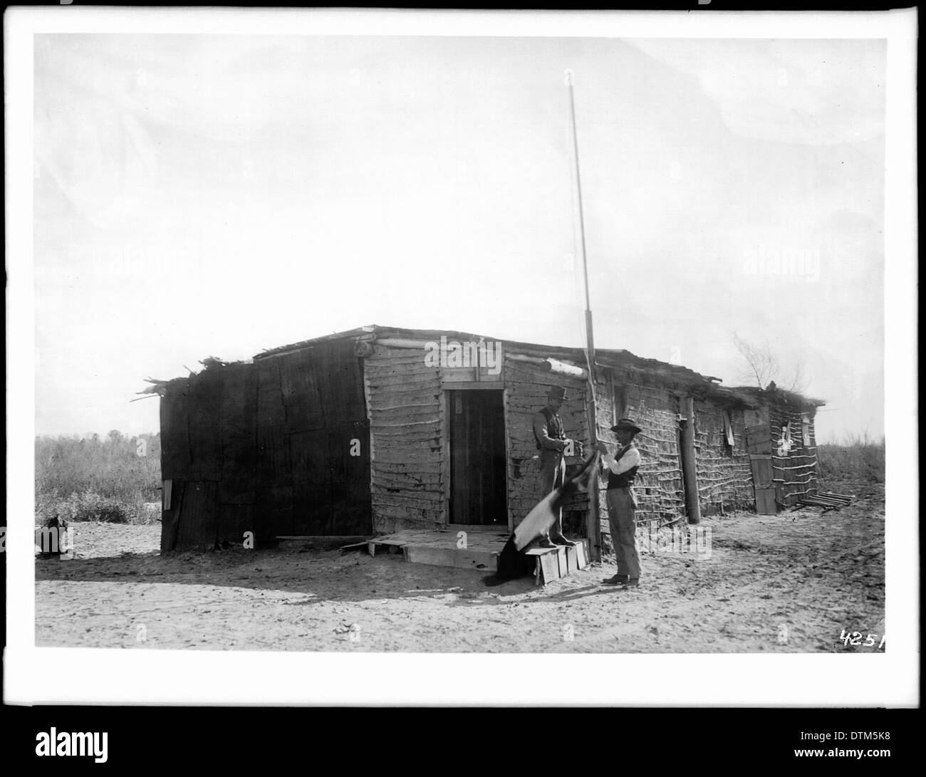 Una fotografia di due uomini che alzano o abbassano una bandiera di fronte alla Custom House messicana vicino Mexicali, scattata intorno al 1910, che illustra il commercio di frontiera e le operazioni doganali dell'inizio del XX secolo. Foto Stock