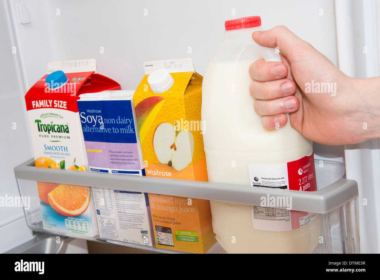 Una mano tirando fuori una bottiglia di latte da una porta frigo Foto Stock