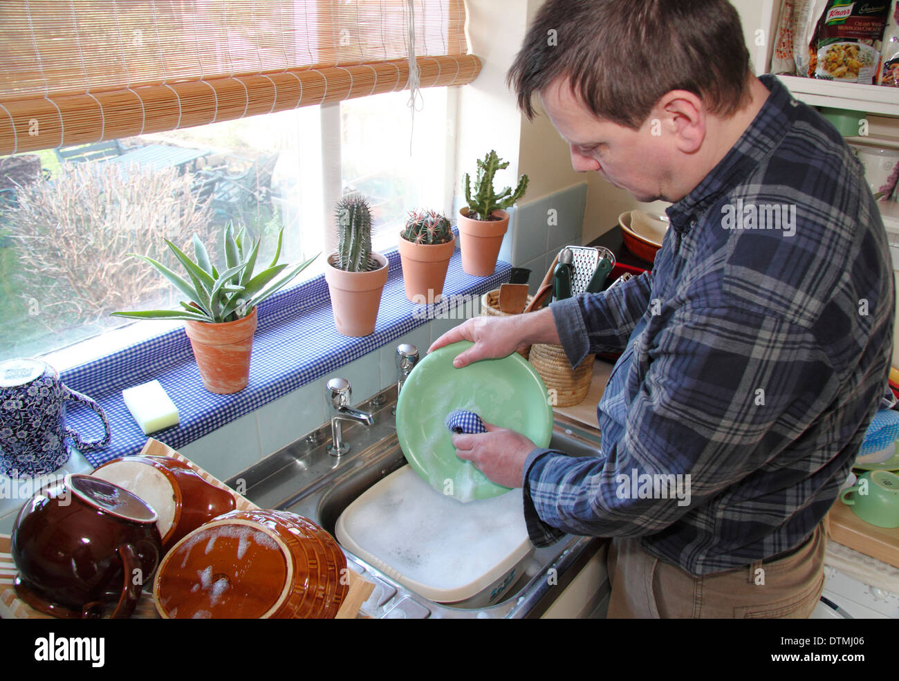 Uomo di lavaggio pentole fino ad un lavello da cucina a casa, England, Regno Unito Foto Stock