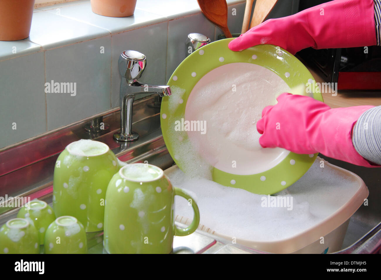 Donna che indossa guanti di gomma per lavare i bicchieri al lavello da cucina a casa Foto Stock