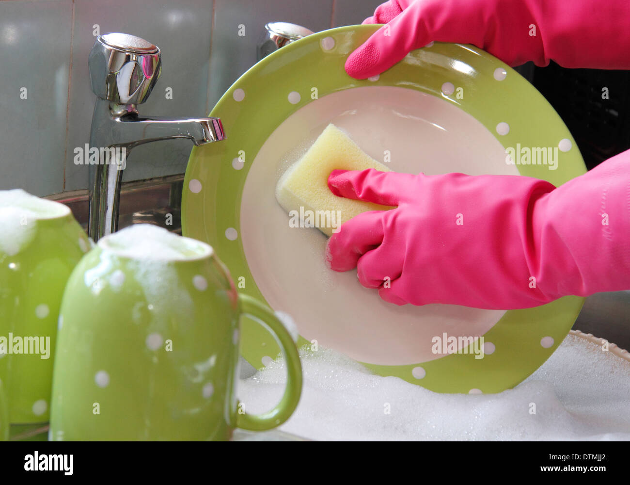Donna che indossa guanti di gomma per lavare i bicchieri al lavello da cucina a casa Foto Stock