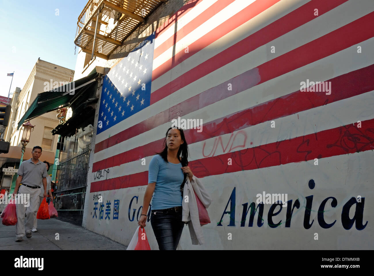 Ragazza cinese a piedi da un murale della bandiera americana su una parete nella Chinatown di San Francisco, California. Foto Stock