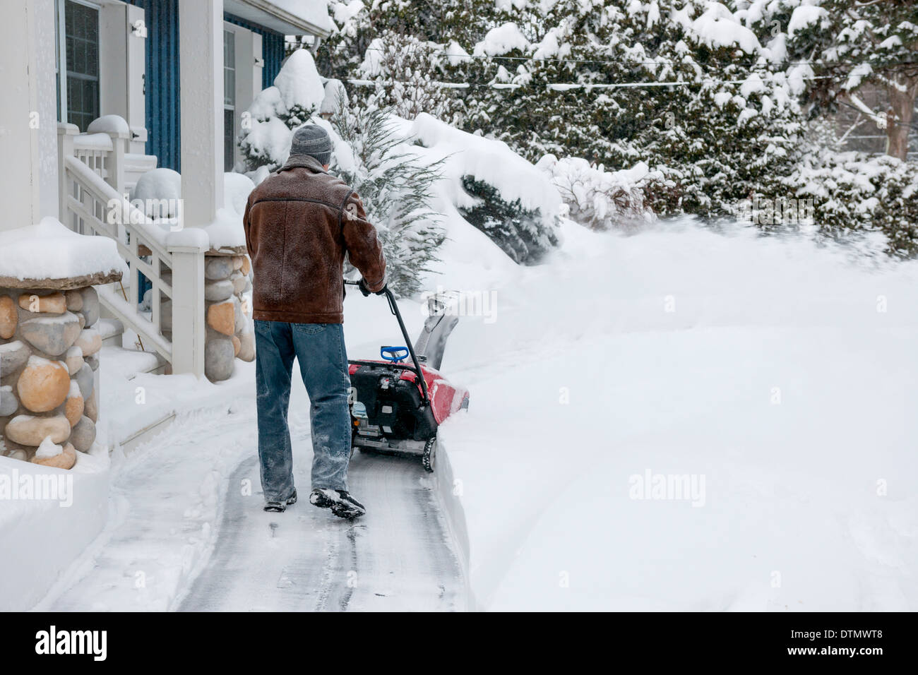 Uomo che utilizza spalaneve per cancellare la neve profonda sul vialetto vicino casa residenziale dopo la nevicata Foto Stock