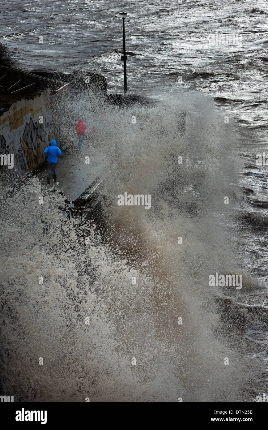 Due persone in esecuzione come onde infrangersi sul lungomare a Weston-Super-Mare Somerset South West England Regno Unito Foto Stock