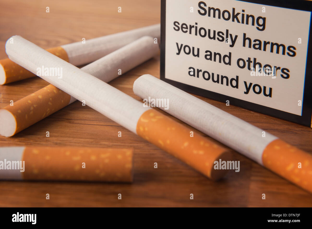 Alcune sigarette e un pacchetto con avvertimento per la salute su una superficie. Foto Stock