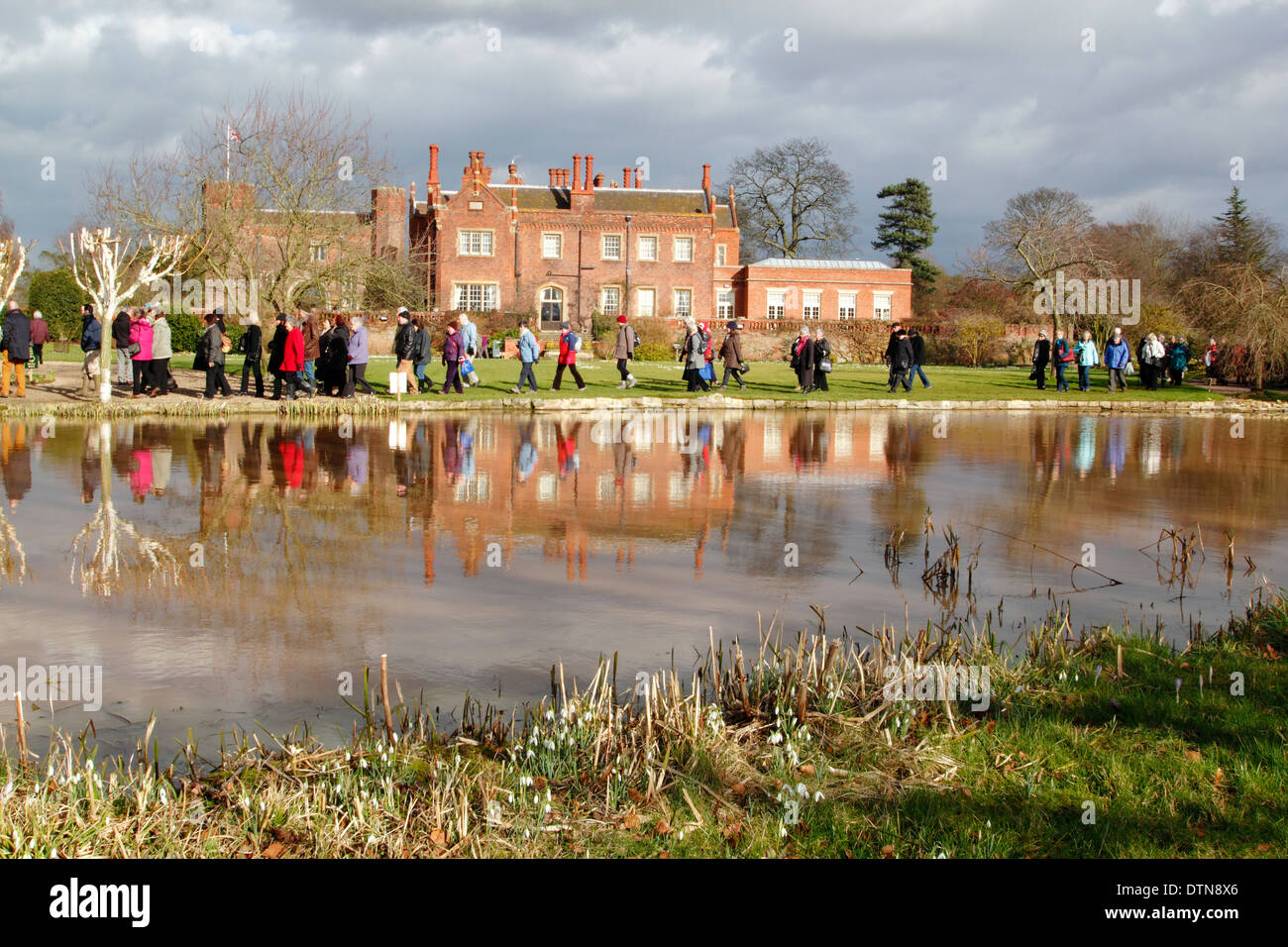 I visitatori a piedi passato Hodsock Priory. Snowdrops in primo piano dal lago nel priorato dei giardini. Foto Stock