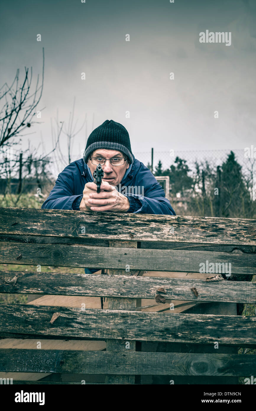 Senior uomo puntando una pistola a voi e nascondersi dietro barricate all'esterno. Foto Stock