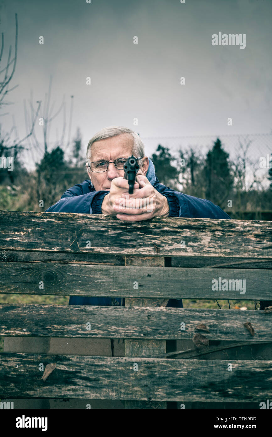 Senior uomo puntando una pistola a voi e nascondersi dietro barricate all'esterno. Foto Stock