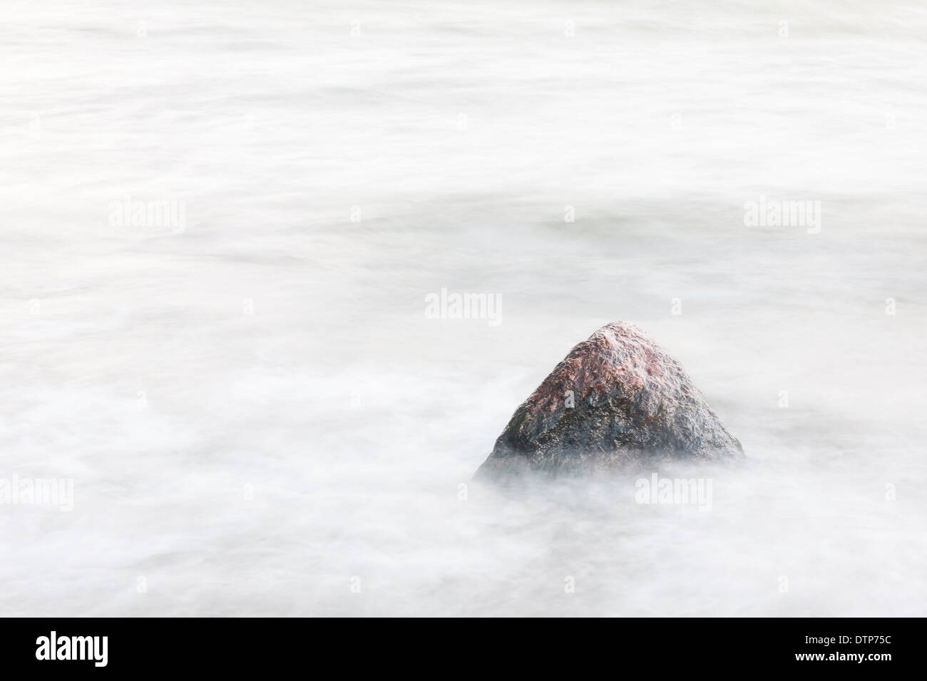 Singola pietra o roccia in un mare sfocato Foto Stock