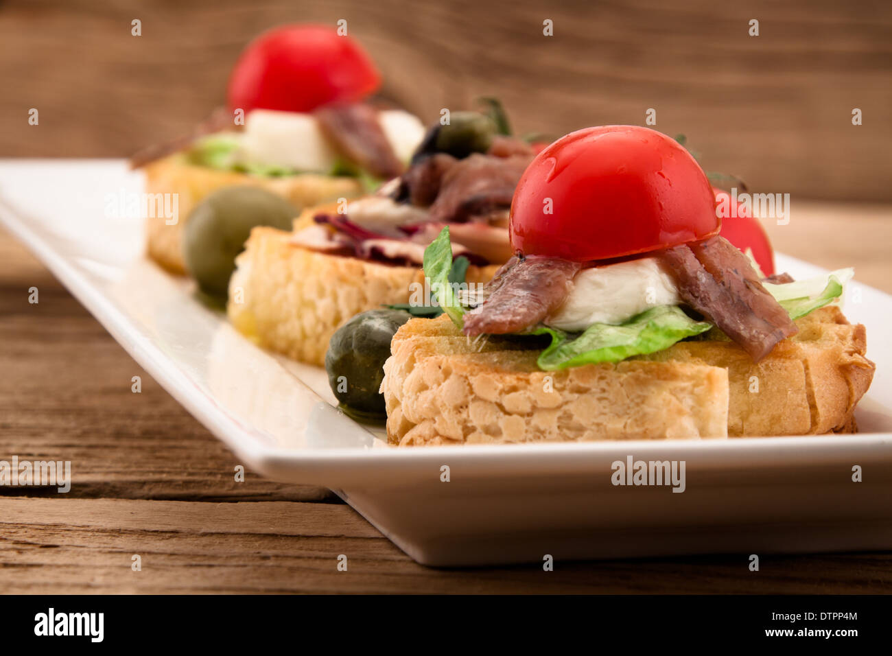 Crostini con mozzarella acciughe e pomodoro sul pannello di legno Foto Stock