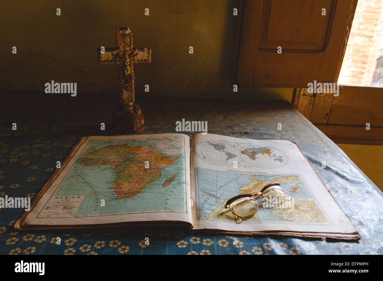 Una vecchia mappa libro è aperto e poggiato su un tavolo con la tovaglia modellato. Vi è una croce con Gesù e bicchieri. Foto Stock