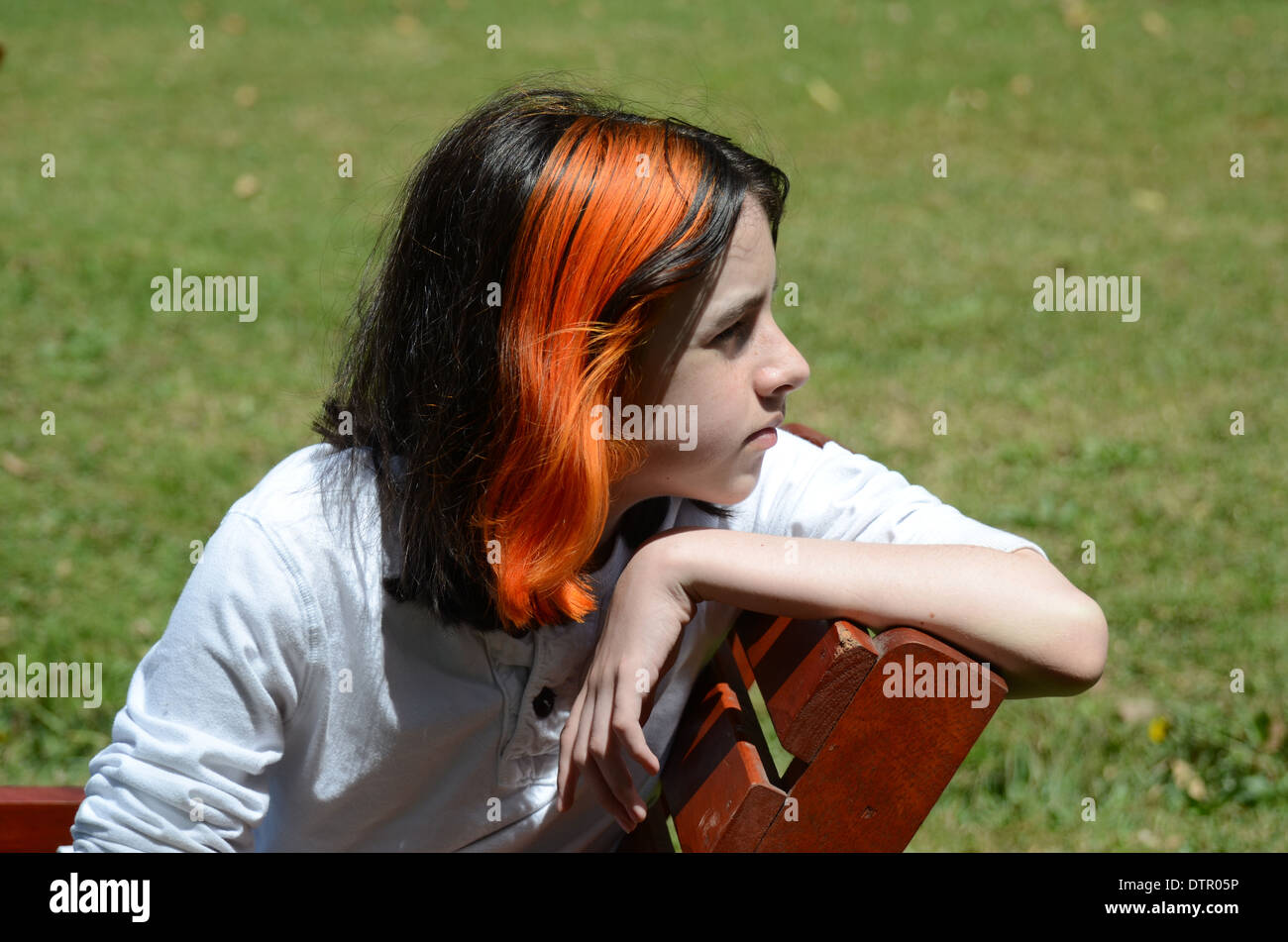 Ragazzo seduto sulla panchina guardando a destra sullo sfondo di erba Foto Stock