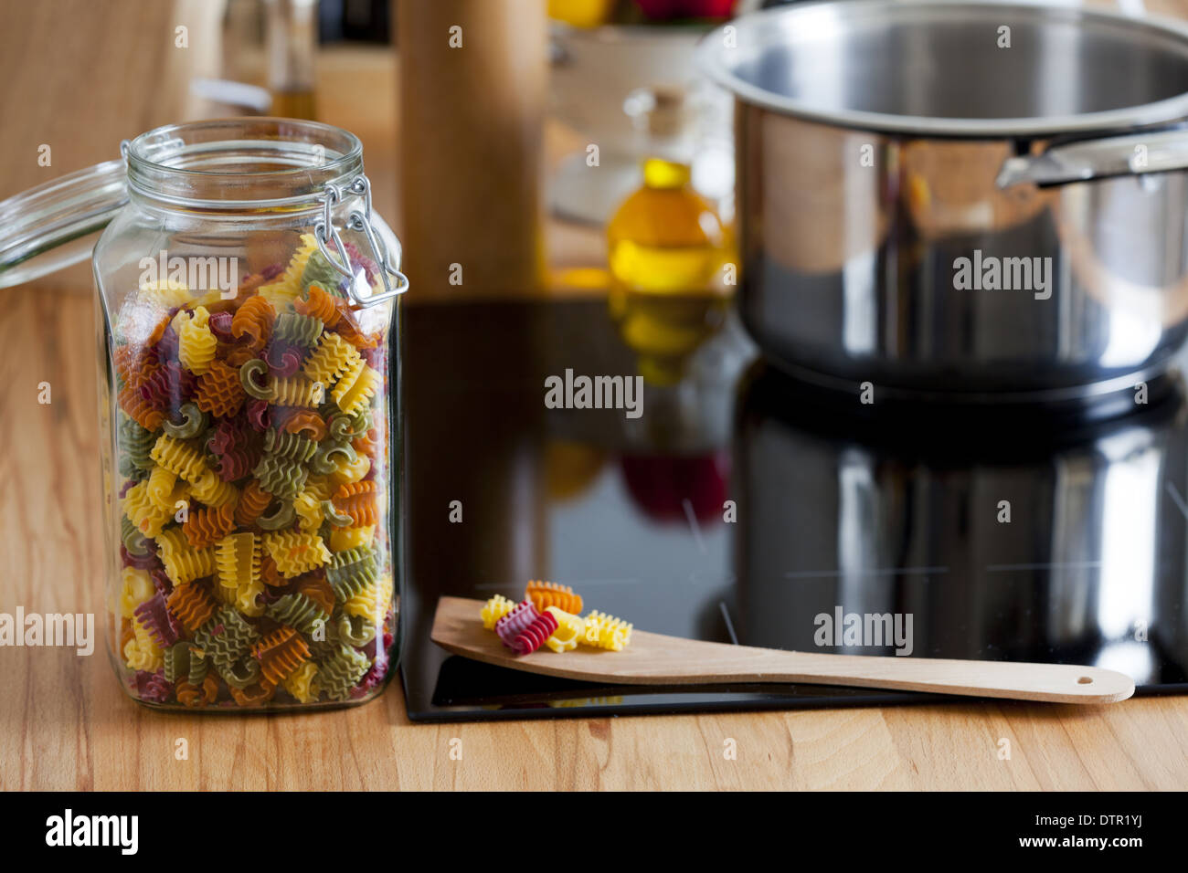 Vaso di storage con pasta colorata e cucchiaio di cottura sul piano di lavoro con copia spazio alla zona a destra dell'immagine Foto Stock