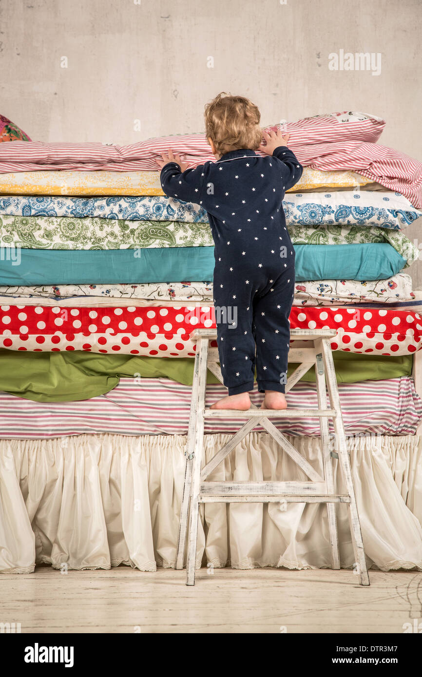 Il bambino si arrampica sul letto con un sacco di trapunte - La principessa sul pisello. Foto Stock