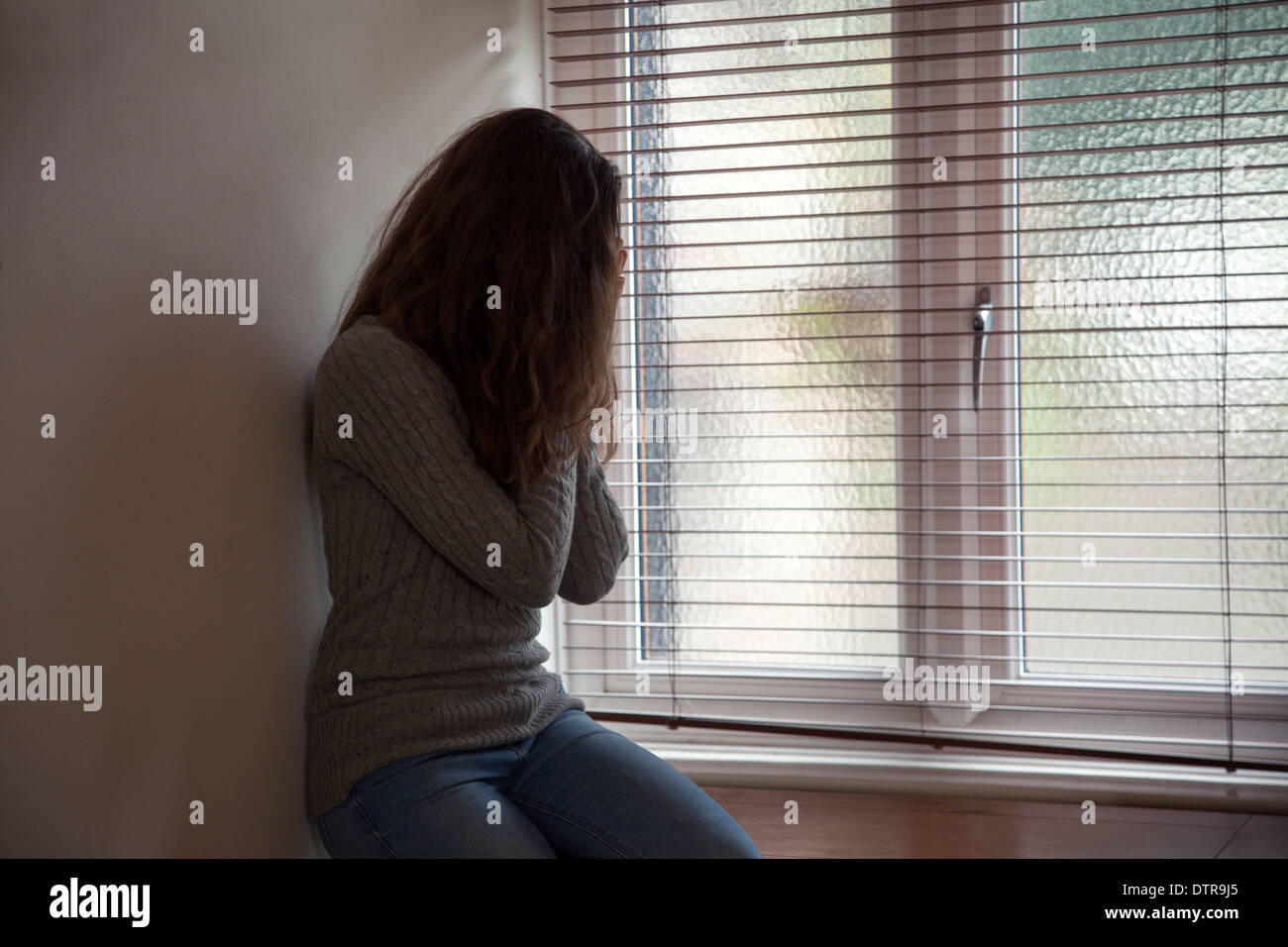 La ragazza con i capelli lunghi e le mani sul suo volto, seduti in una finestra a casa. Punto di vista laterale. Foto Stock