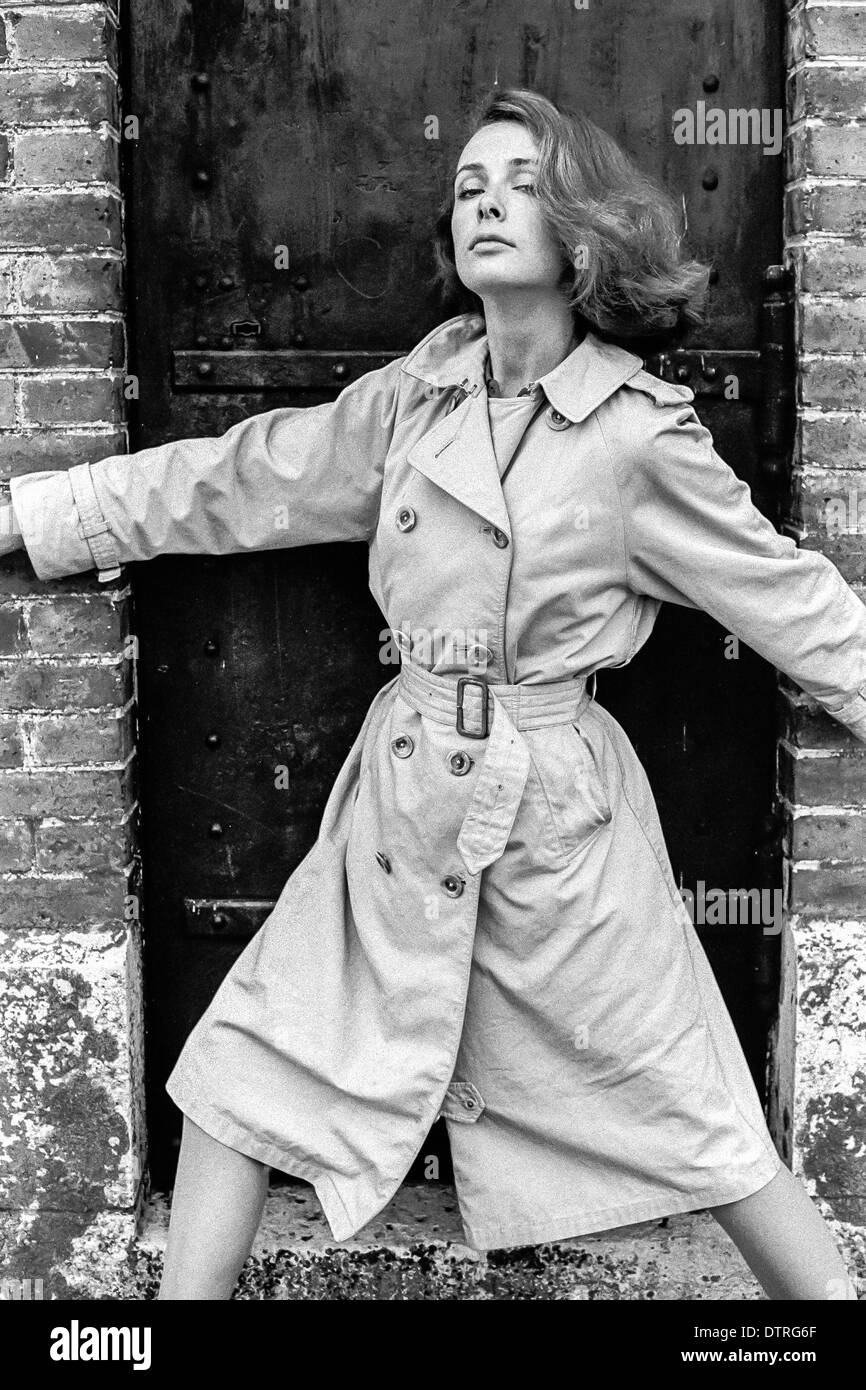 Negli anni sessanta la moda modello con un impermeabile in posa contro una porta nera Foto Stock