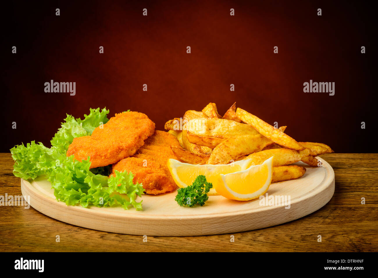 Ancora in vita con il tradizionale pesce e patatine, limoni, su una lastra di legno Foto Stock