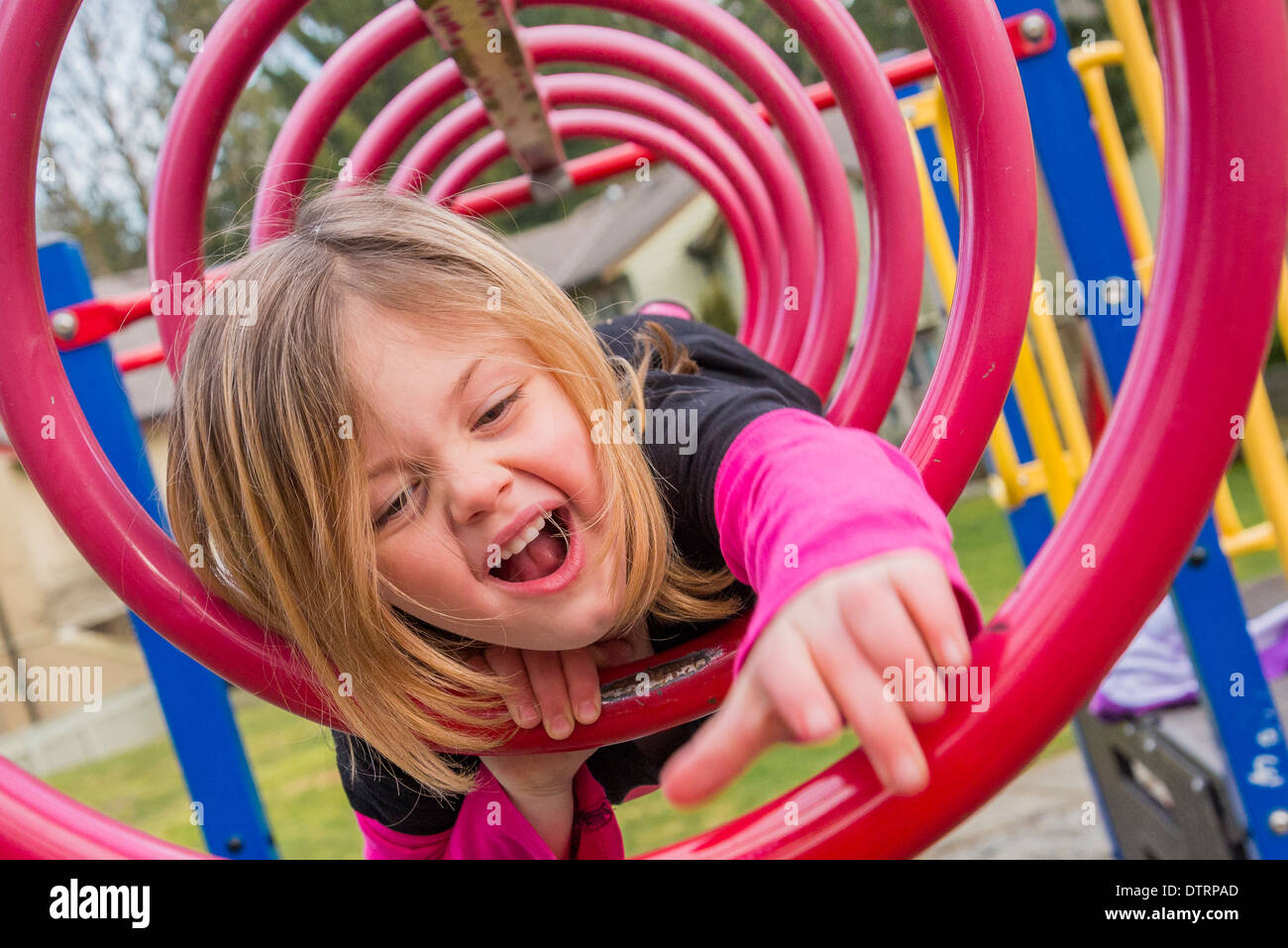 Ragazza giovane si arrampica attraverso barre circolari in parco giochi Foto Stock