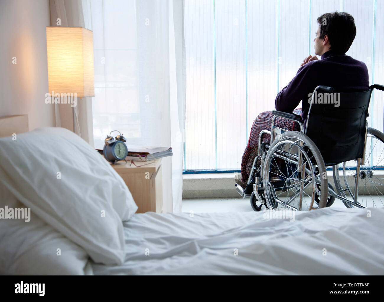 Malinconici uomo caucasico in sedia a rotelle dalla finestra Foto Stock