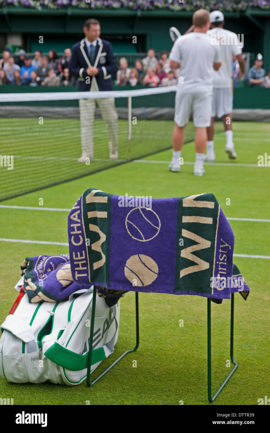 Due maschi i giocatori di tennis a net con arbitro in primo piano una sedia con sacchetti di giocatori e campionati di Wimbledon asciugamano appeso sopra indietro Foto Stock