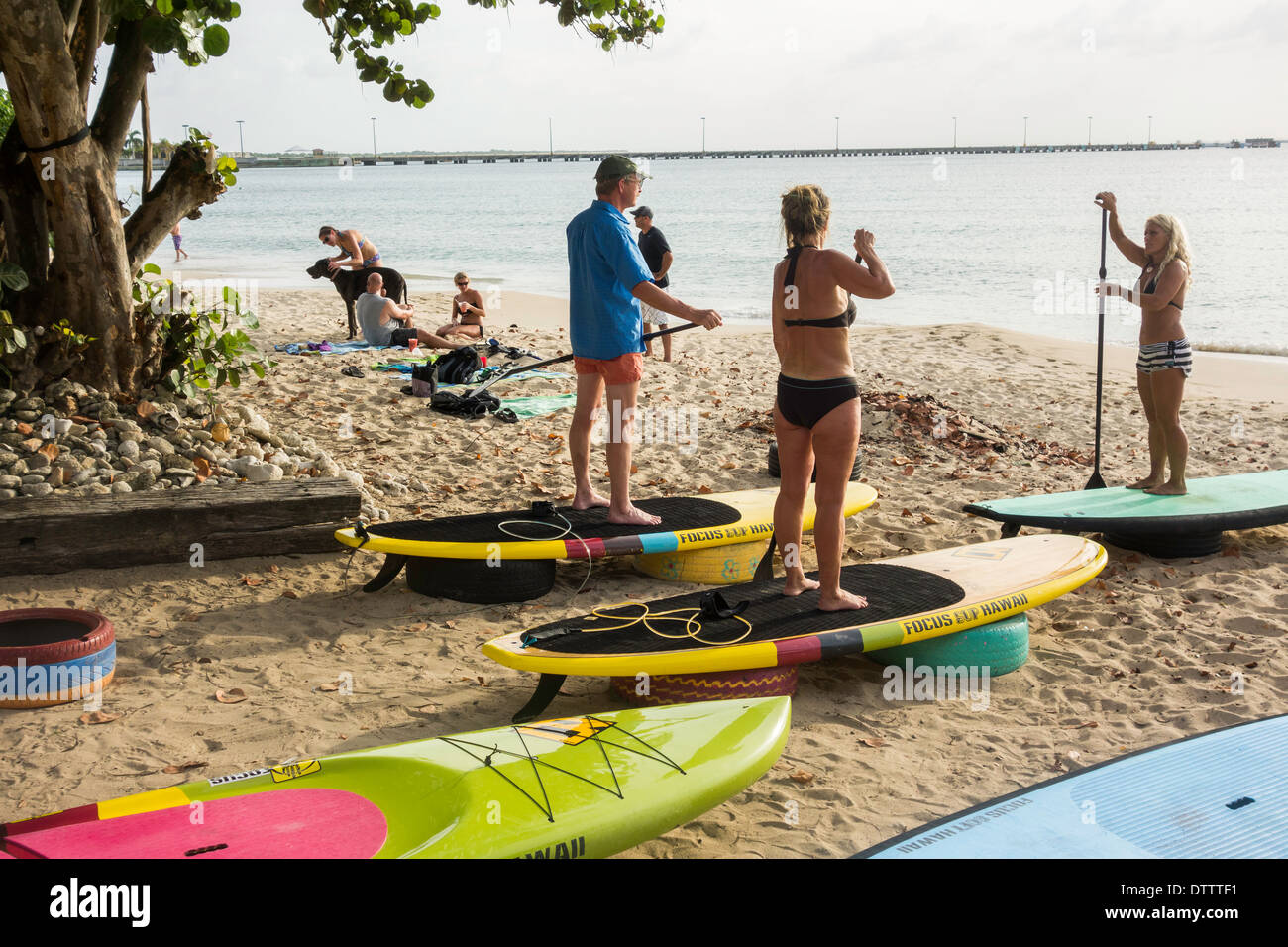 Una donna bionda istruttore insegna una classe in stand up paddle di salire a bordo di un uomo caucasico e la donna nel loro 30s. Sy. Croix, U.S. Isole Vergini. Foto Stock