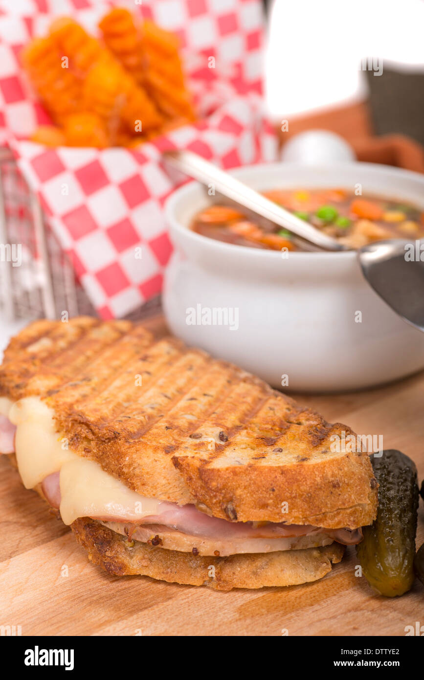 Deliziosi panini fatti con prosciutto, carne di maiale e il formaggio svizzero è servita con una zuppa di verdure e sottaceti e la patata dolce patate fritte Foto Stock
