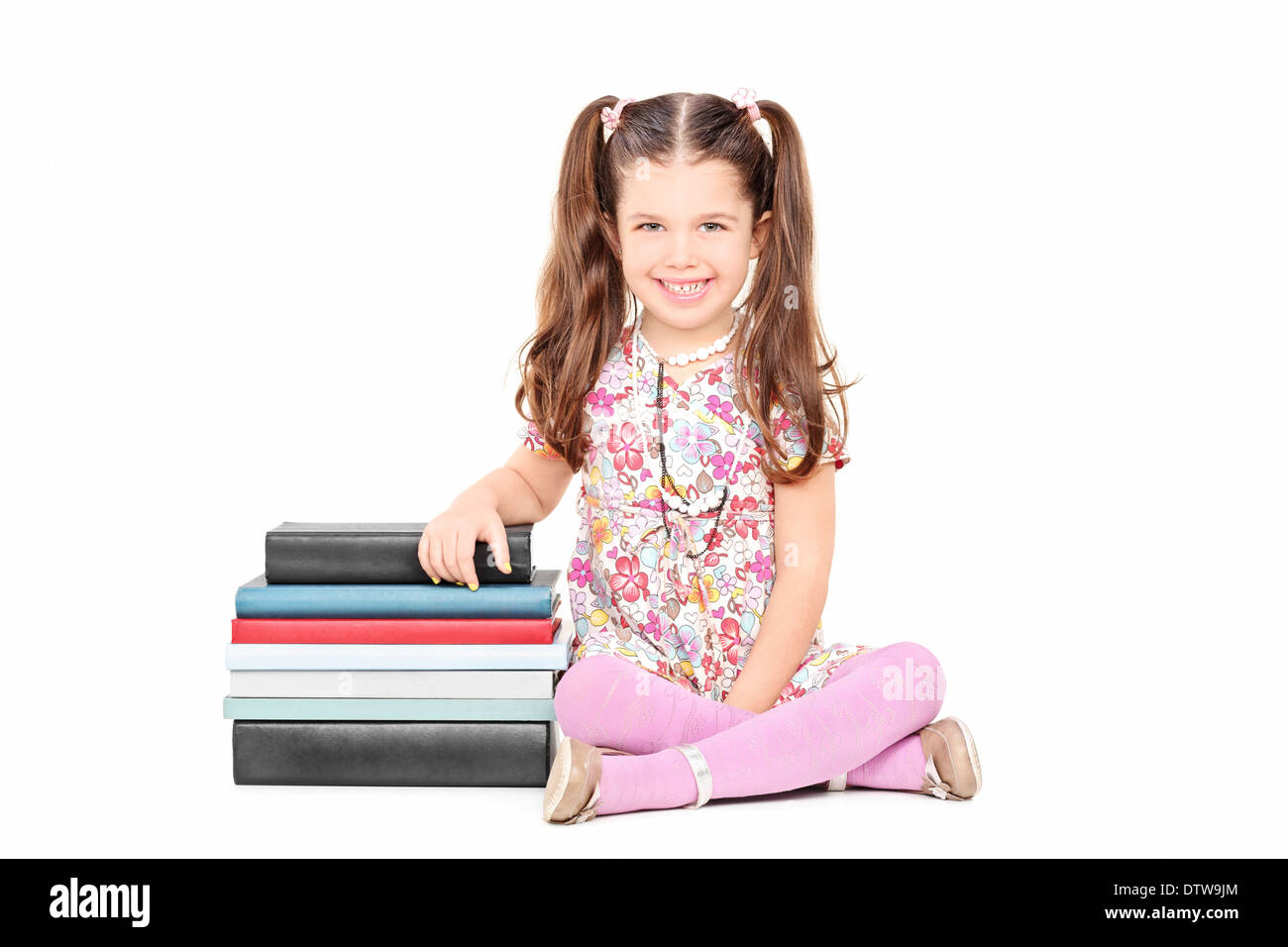 Incantevole piccola ragazza seduta accanto a una pila di libri Foto Stock